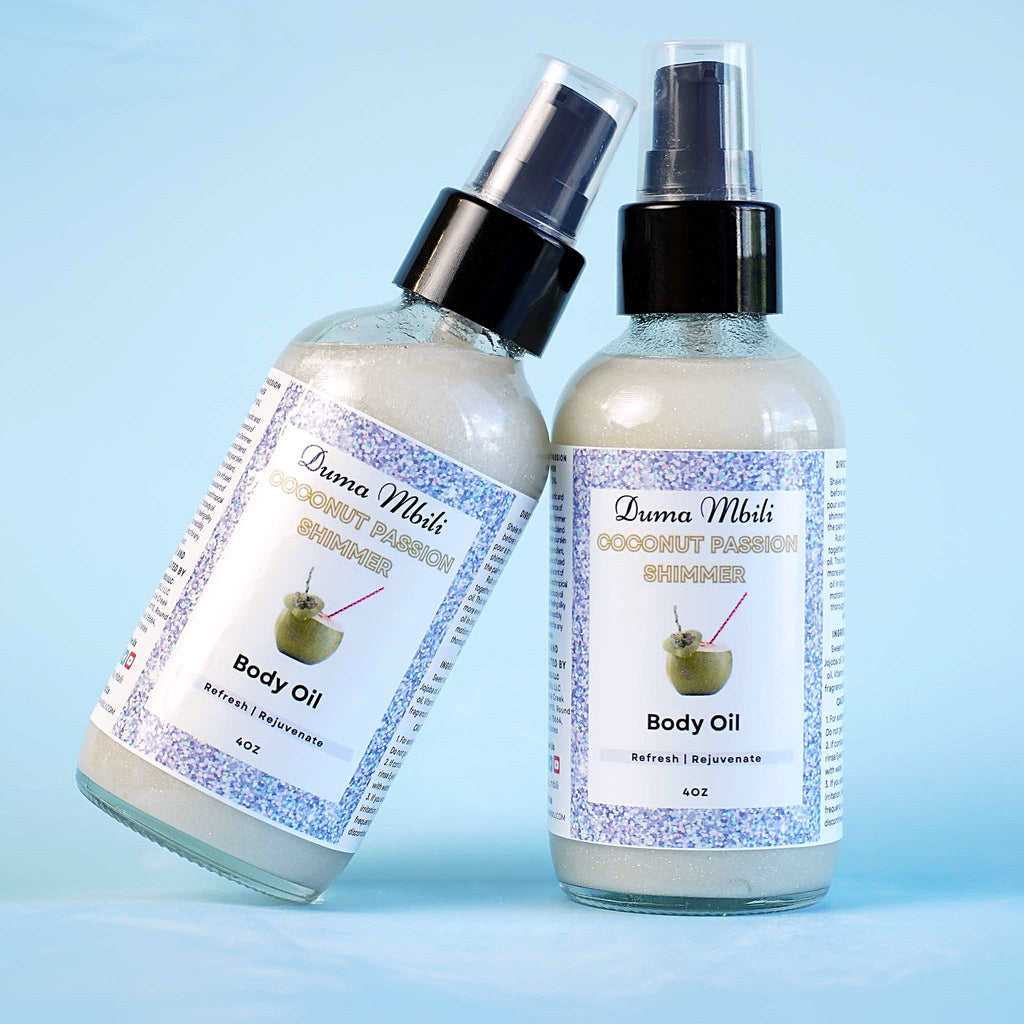 Close-up of two Duma Mbili Coconut Passion Shimmer Body Oil bottles on a blue background.